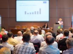 A speaker gives a talk at a conference to a crowd of people.