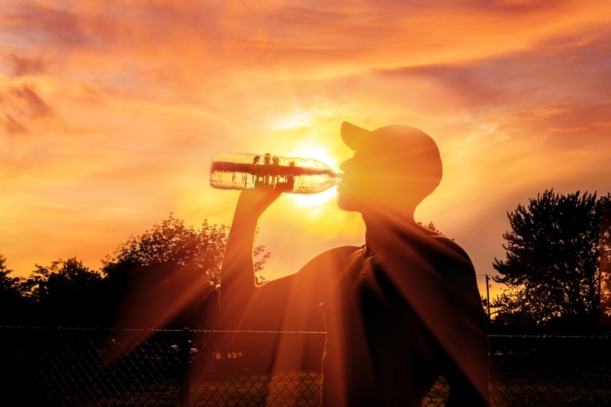 Silhouette of a man drinking water in a wooded area. Strong sunlight beams from the background. 